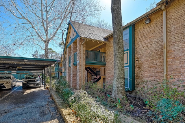 view of property exterior featuring brick siding, a carport, driveway, and a shingled roof