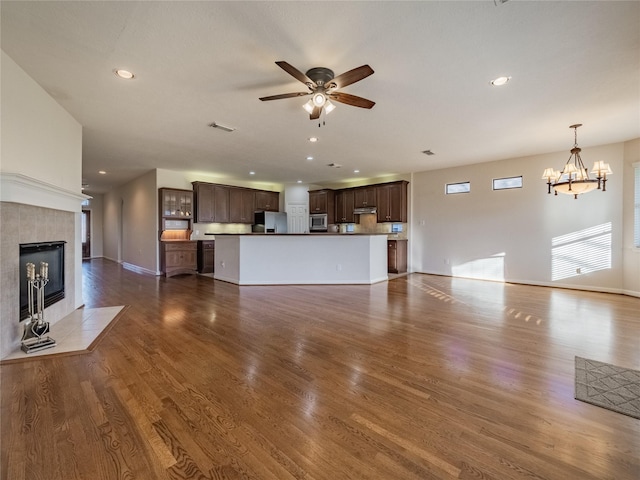 unfurnished living room with wood finished floors, baseboards, recessed lighting, a tiled fireplace, and ceiling fan with notable chandelier