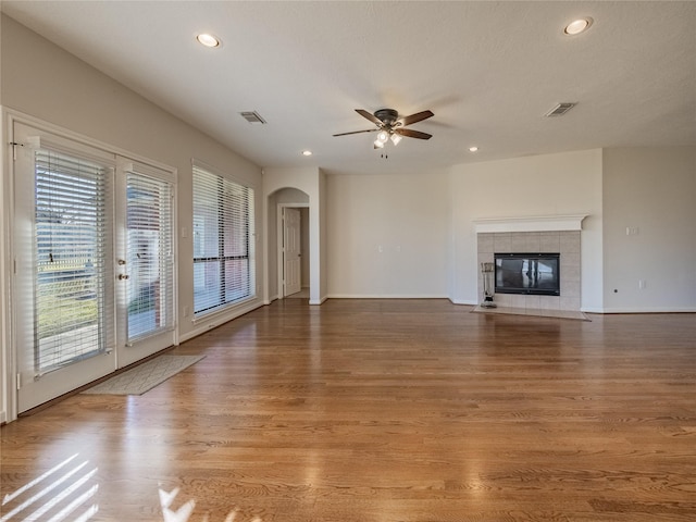 unfurnished living room with a tiled fireplace, wood finished floors, visible vents, and arched walkways