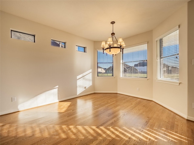 spare room with baseboards, an inviting chandelier, and wood finished floors