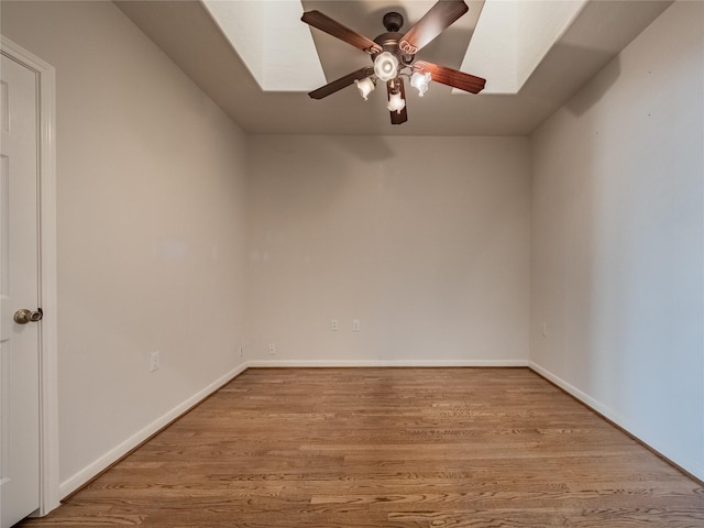 spare room featuring a ceiling fan, a skylight, wood finished floors, and baseboards