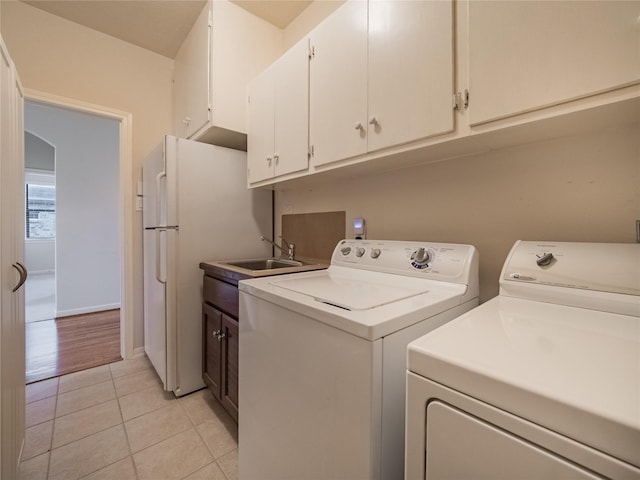 washroom featuring light tile patterned flooring, cabinet space, arched walkways, a sink, and washer and clothes dryer