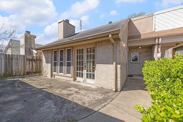 rear view of house featuring fence, a chimney, french doors, a patio area, and brick siding