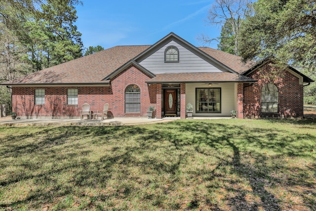 view of front of home with brick siding, a front yard, and roof with shingles