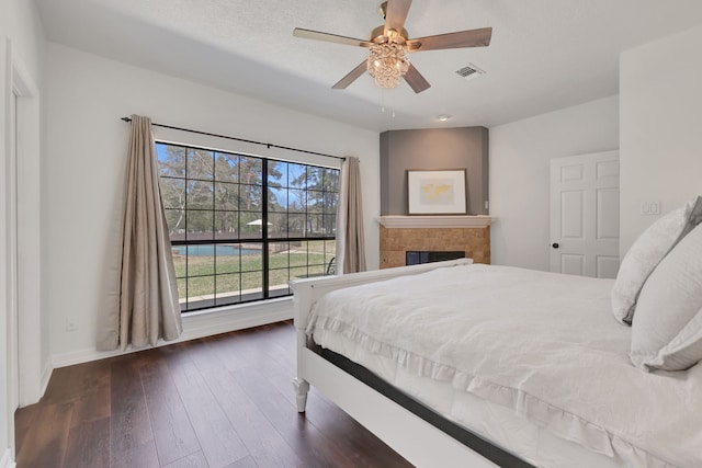 bedroom with visible vents, dark wood-type flooring, a textured ceiling, a fireplace, and ceiling fan