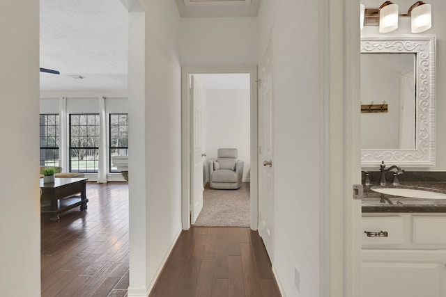 corridor featuring dark wood finished floors, baseboards, and a sink