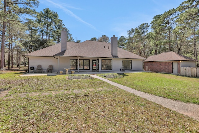 back of house featuring a lawn, a shingled roof, a chimney, and a patio area