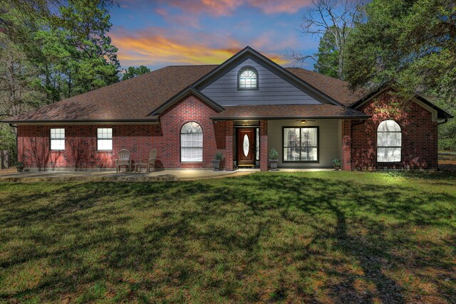 view of front of home featuring a front yard, brick siding, and roof with shingles