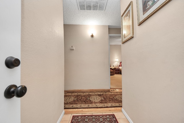 hallway featuring tile patterned floors, visible vents, baseboards, and a textured ceiling