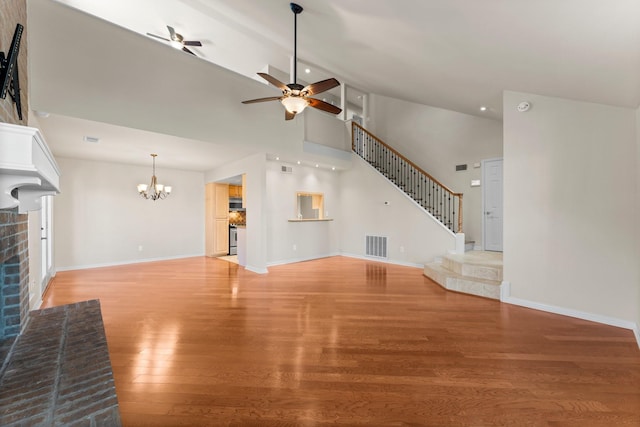 unfurnished living room with stairway, visible vents, a fireplace, ceiling fan with notable chandelier, and light wood-type flooring