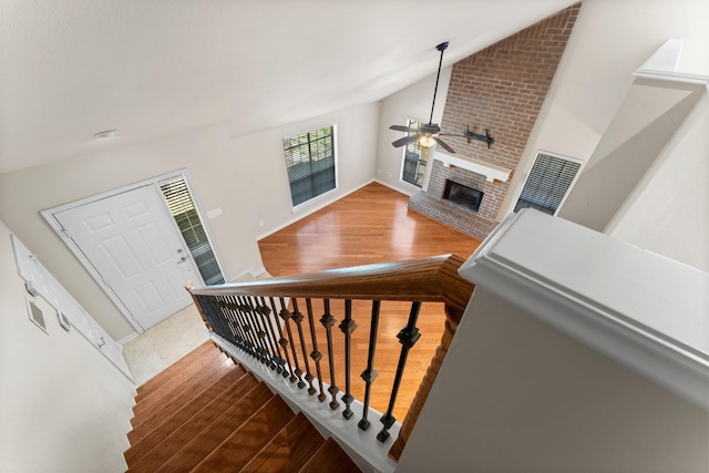 stairs with wood finished floors, baseboards, a brick fireplace, ceiling fan, and vaulted ceiling