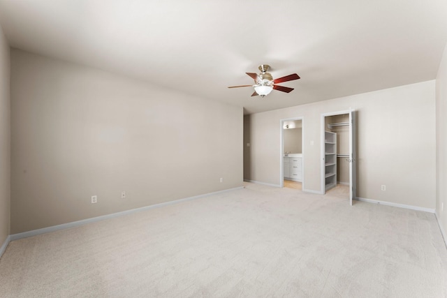 unfurnished bedroom with a closet, baseboards, light colored carpet, ceiling fan, and a spacious closet