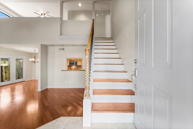 stairs featuring a notable chandelier, visible vents, baseboards, and wood finished floors