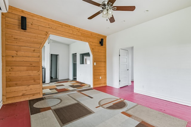 interior space with wooden walls, baseboards, an AC wall unit, wood finished floors, and a ceiling fan