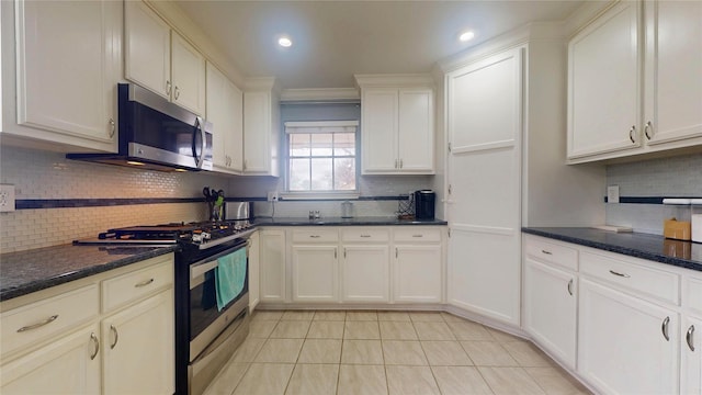 kitchen featuring dark stone countertops, light tile patterned floors, decorative backsplash, white cabinets, and appliances with stainless steel finishes