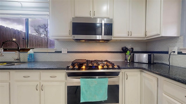 kitchen featuring decorative backsplash, white cabinets, stainless steel appliances, and a sink