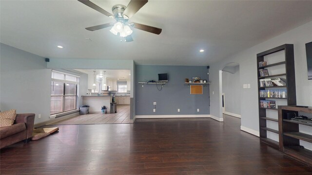 living room with a ceiling fan, wood finished floors, arched walkways, and baseboards