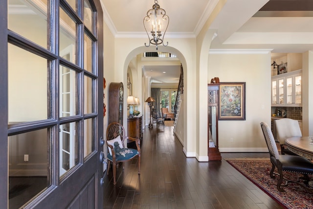 entryway featuring baseboards, dark wood finished floors, arched walkways, ornamental molding, and a notable chandelier