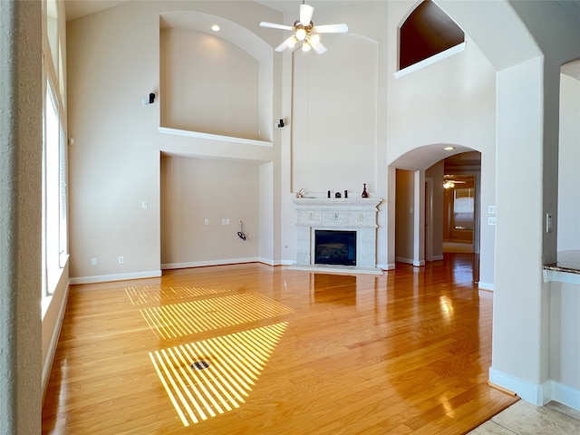 unfurnished living room featuring baseboards, ceiling fan, a fireplace with flush hearth, light wood-style floors, and arched walkways