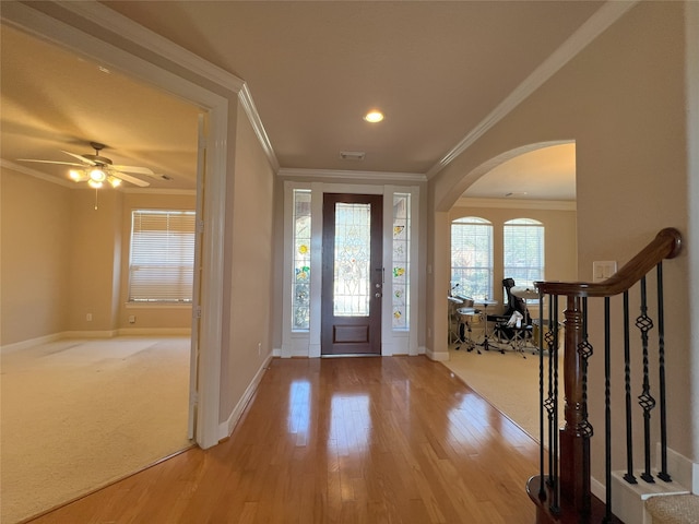 foyer featuring baseboards, light wood-style flooring, arched walkways, stairs, and crown molding