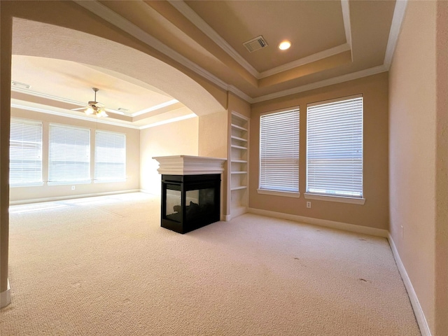 unfurnished living room with built in shelves, a tray ceiling, a multi sided fireplace, and ornamental molding