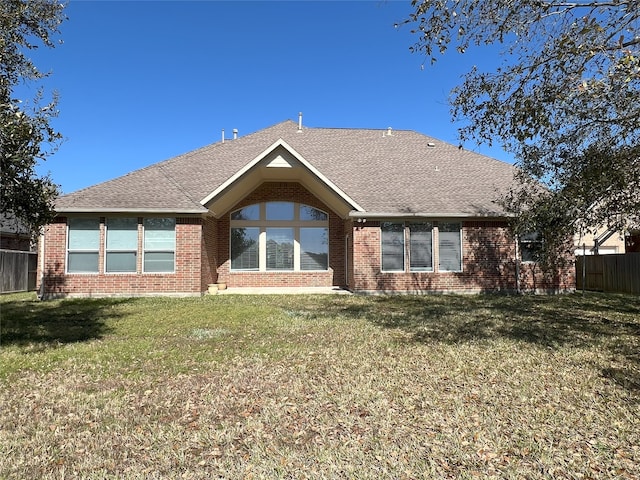 back of house featuring brick siding, roof with shingles, a yard, and fence