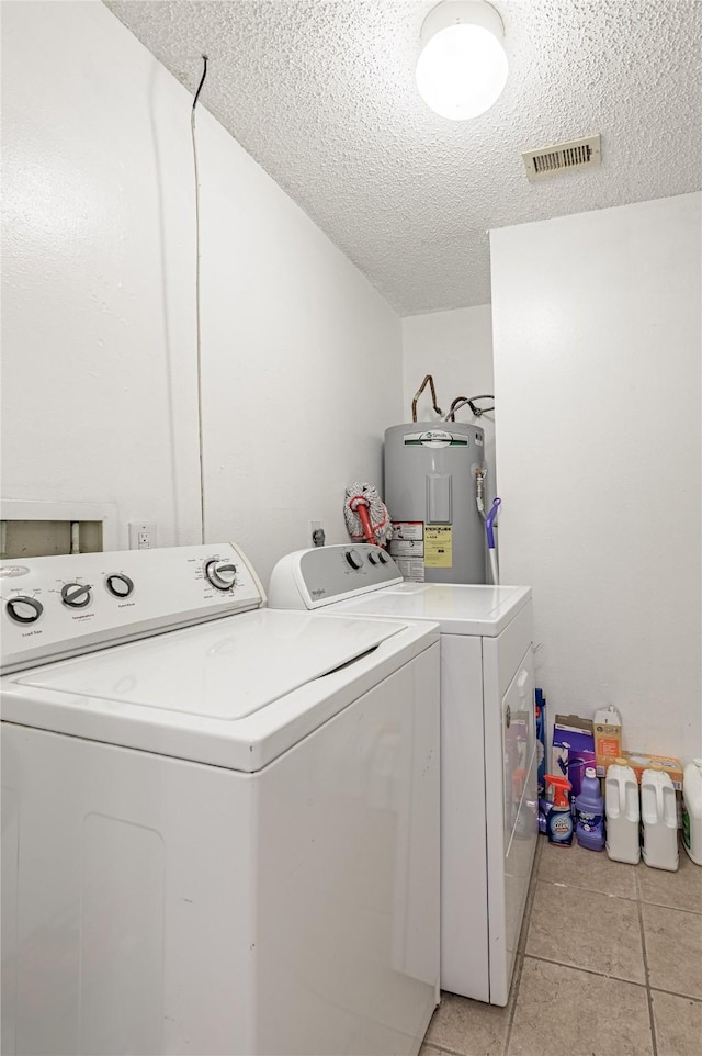 clothes washing area featuring visible vents, electric water heater, laundry area, a textured ceiling, and separate washer and dryer