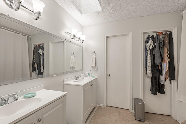 bathroom featuring a textured ceiling, tile patterned floors, two vanities, and a sink