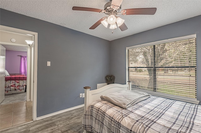 bedroom featuring baseboards, a textured ceiling, wood finished floors, and a ceiling fan