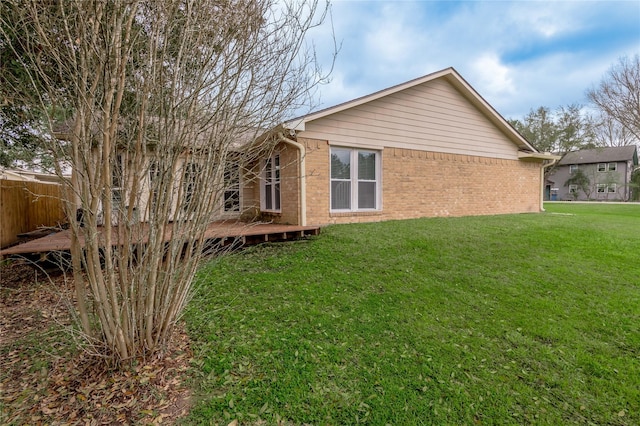 back of property featuring brick siding, a wooden deck, a yard, and fence