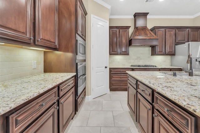 kitchen featuring premium range hood, appliances with stainless steel finishes, crown molding, light tile patterned floors, and light stone countertops