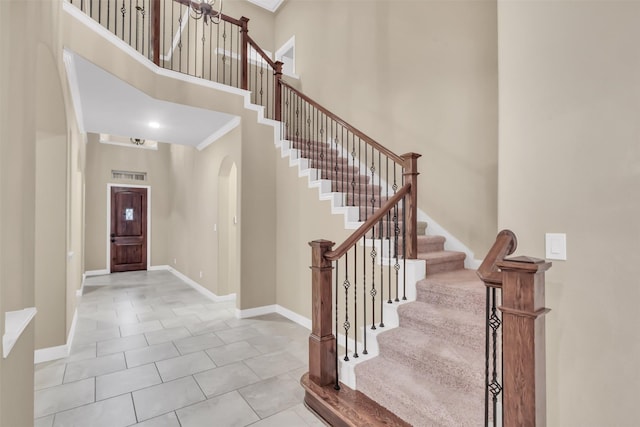 tiled foyer entrance featuring visible vents, baseboards, arched walkways, stairs, and a towering ceiling