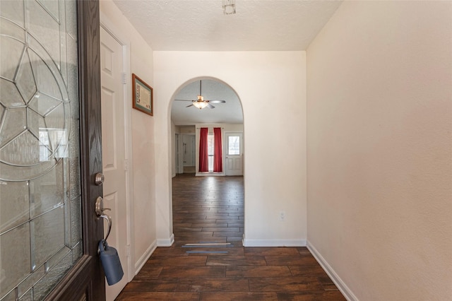 entrance foyer with a textured ceiling, dark wood finished floors, arched walkways, baseboards, and ceiling fan