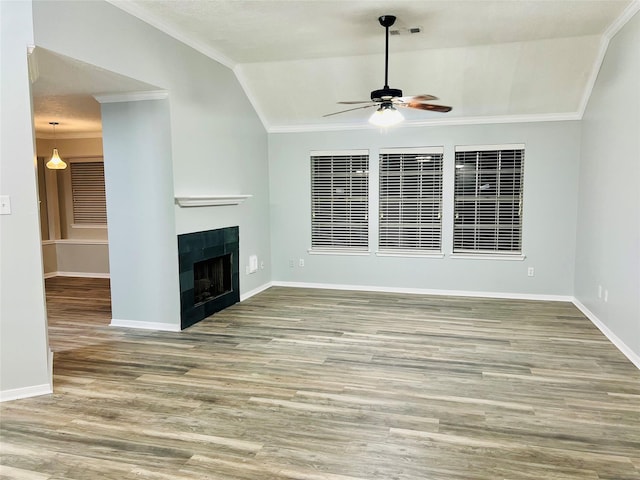 unfurnished living room featuring crown molding, baseboards, lofted ceiling, a tile fireplace, and wood finished floors