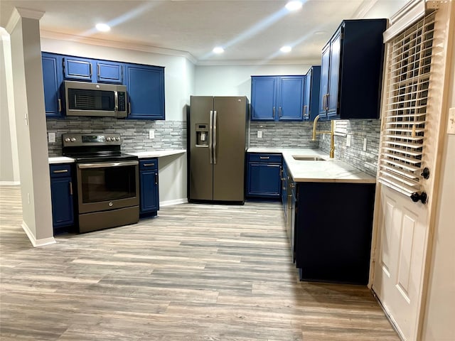 kitchen with blue cabinetry, ornamental molding, a sink, appliances with stainless steel finishes, and light wood-type flooring