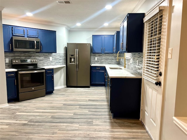 kitchen with blue cabinetry, ornamental molding, light wood-style flooring, appliances with stainless steel finishes, and a sink