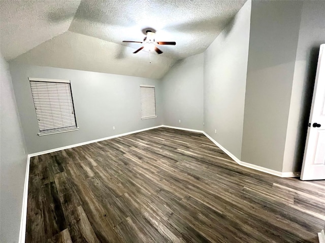 spare room featuring baseboards, a textured ceiling, dark wood-style floors, and vaulted ceiling