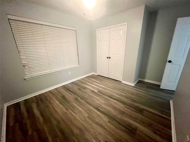 unfurnished bedroom with baseboards, dark wood-style flooring, and a closet