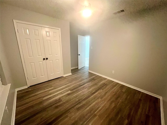 unfurnished bedroom with visible vents, a textured ceiling, a closet, baseboards, and dark wood-style flooring