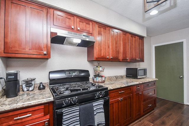 kitchen with light stone counters, gas stove, dark wood-style flooring, under cabinet range hood, and stainless steel microwave