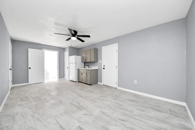 unfurnished living room with a ceiling fan, baseboards, and a sink