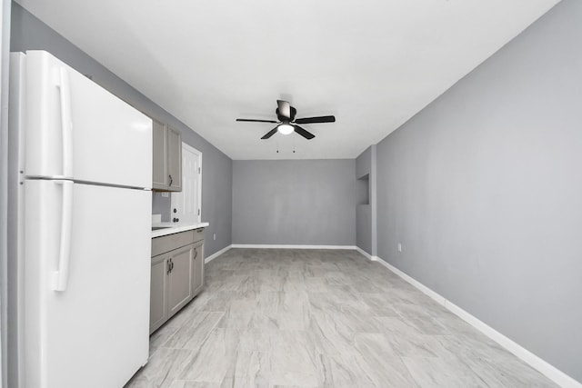 kitchen with a ceiling fan, gray cabinets, freestanding refrigerator, light countertops, and baseboards