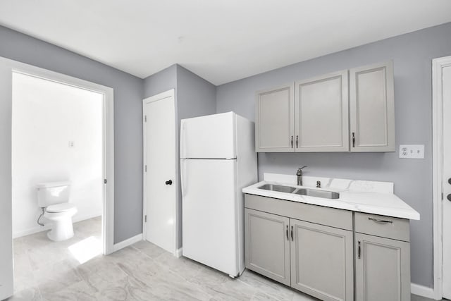 kitchen with baseboards, light countertops, gray cabinets, freestanding refrigerator, and a sink