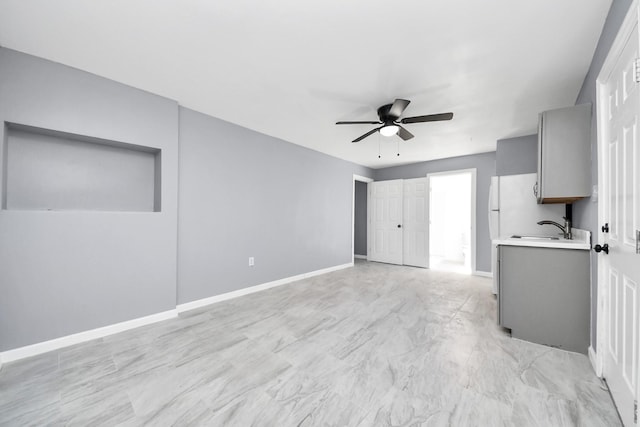 unfurnished living room featuring a sink, baseboards, marble finish floor, and ceiling fan