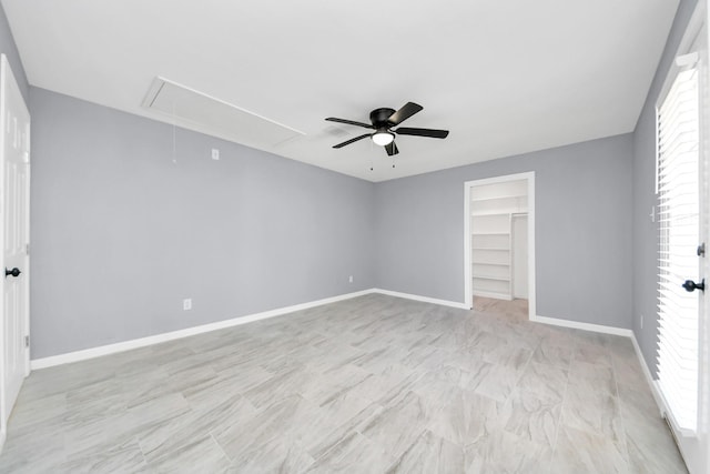 unfurnished bedroom featuring a spacious closet, baseboards, attic access, a closet, and a ceiling fan