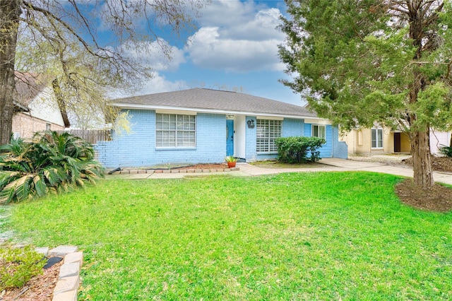 ranch-style home with a front yard, fence, driveway, roof with shingles, and brick siding