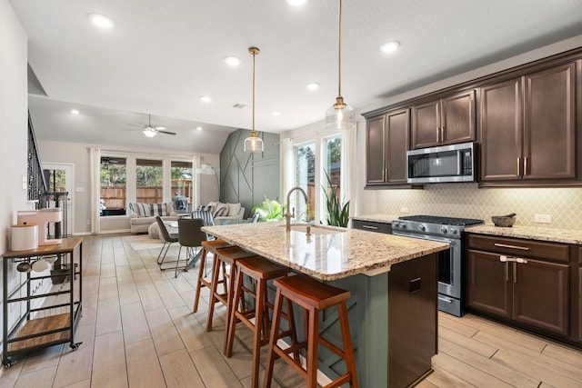 kitchen with wood finish floors, a sink, dark brown cabinetry, appliances with stainless steel finishes, and backsplash