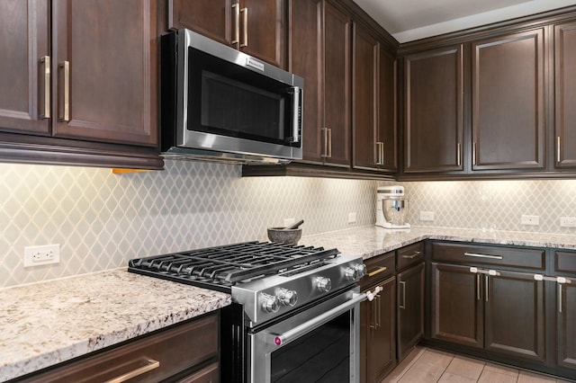 kitchen featuring backsplash, dark brown cabinets, appliances with stainless steel finishes, and light stone countertops