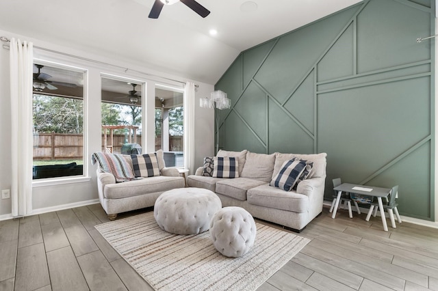 living area with baseboards, lofted ceiling, ceiling fan, a decorative wall, and light wood-type flooring