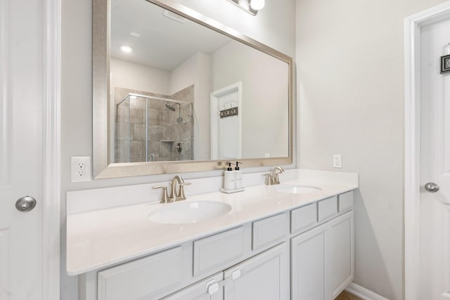 bathroom with a shower stall, double vanity, baseboards, and a sink